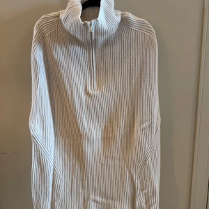 Ärmlös benvit ribbstickad half zip tröja - Ribbstickad benvit ärmlös tröja i over size modell med hög krage och half zip-dragkedja. 