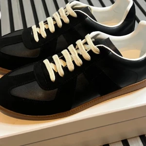 Svarta sneakers Maison Margiela - Maison Margiela sneakers i svart skinn och mocka med kontrasterande vita snören och klassisk gummisula i beige. Snygg retrostil med rund tå och platt sula, perfekt för dig som gillar minimalistisk design med en twist.