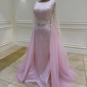 Ljusrosa glittrig långklänning med släp - Ljusrosa/baby rosa långklänning med glittriga pärldetaljer och transparenta långa ärmar. Klänningen har ett släp i tyll och figurnära passform. Passar storlek XS och S. Perfekt för bal, fest bröllop! Kläningen är customised från Turkiet och är endast använd en gång av mig på ett bröllop. Kläningens totala pris var 3500 kr (+200 med frakt) och jag säljer den nu för 2500 kr så får någon annan få möjligheten att få bära denna vackra kläningen!!😍