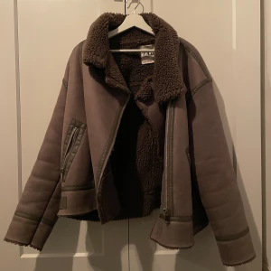 Brun teddyjacka från Zara - Säljer en brun grå teddyjacka från Zara med mysigt foder och bred krage. Jackan har dragkedjor på sidorna och uppe vid kragen finns ett band som man kan justera. Otroligt varm och perfekt inför hösten/vinter!