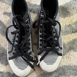 Randiga Adidas sneakers i svartvitt - Snygga Adidas sneakers i svartvitt randigt tyg med svarta snören och svart sula. Modellen är mellanhög och har klassisk rund tå. Perfekta för dig som gillar en unik och stilren look. Märke syns på sidan och insidan av skon.