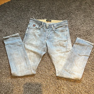 Ljusblå jeans från Jack & Jones  - Säljer ett par ljusblå jeans från Jack & Jones, modell Jeans Intelligence. Jeansen är tillverkade i bomull och har snygga slitningar för en avslappnad look.