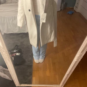Beige kappa med bälte från Zara XS - Snygg beige kappa från Zara i storlek XS. Modellen är rak med knappar framtill och ett matchande bälte i midjan. Jackan har långa ärmar och är tillverkad i ett mjukt material som känns lyxigt. Perfekt för dig som vill ha en stilren och trendig look.Aldrig andvänd pris lapp kvar ändå stor i storleken 