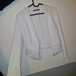 Kavaj jacka - Snygg vit kavajjacka från Gina Tricot med croppad passform och långa ärmar. Jackan har en öppen front och markerade sömmar för en stilren look. Perfekt för att lyfta din outfit med en fräsch och clean vibe. Den har legat i en kasse i källaren därför behöver den tvättas pga lite fläckar här o där.
