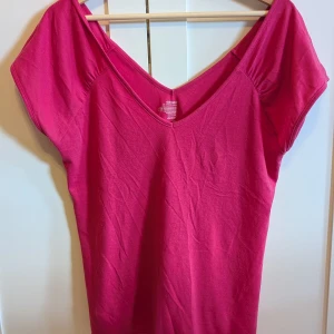 Ceriserosa v-ringad topp Old Navy - Säljer en ceriserosa topp från Old Navy med v-ringning och korta ärmar. Toppen är i mjuk bomull och har en enkel, stilren design som är lätt att matcha. Perfekt för dig som gillar färg och vill ha en bekväm vardagstopp.