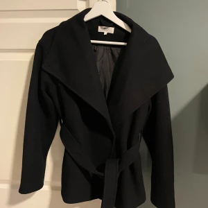 Svart kappa från Gina Tricot med bälte - Kappa från Gina använd en gång pga den passar inte mig köpt nu i oktober ny pris 600kr, byte kan vara intressant! Hör av dig för frågor😊