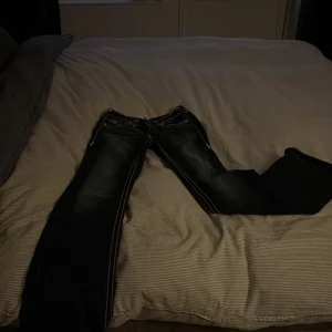 True Religion Becca Bootcut Jeans - Säljer ett par True Religion Becca Mid Rise Bootcut jeans i mörkblå denim med kontrasterande rosa och vita sömmar. Klassiska fickor med kopparfärgade knappar och detaljerad bakficka. Snygg bootcut-modell som ger en cool och tidlös look.använda 2 gånger å de kosta 2600