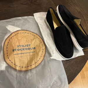 Svarta mockaloafers Stilig Stockholm - Snygga svarta loafers från Stiligt Stockholm i mjuk mocka med vit platt sula. Köpte fel storlek, dom är helt nya och fräscha och redo för att användas köpta för 800