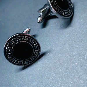 Prisförslag- 1 par Svarta och silver manschettknappar - Runda manschettknappar i silverfärg med svart centrum och en snygg grekisk-inspirerad bård runt kanten. Perfekta för att ge skjortan en extra touch av stil och elegans.