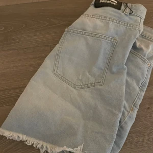 Ljusblå jeanskjol från Dr Denim - Säljer en ljus blå kjol  från Dr Denim med råa, fransiga kanter och slitningar framtill. Klassisk femficksmodell och hög midja. Perfekta för sommaren och ger en avslappnad vibe.