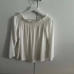 Vit offshoulder blus - Säljer en vit offshoulder blus från Gina Tricot med smockad resår och söt volang upptill. Blusen har långa, vida ärmar och är tillverkad i ett mjukt, lätt material som ger ett flowy intryck. Perfekt för dig som gillar romantisk och trendig stil🤍