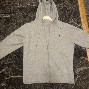 Grå hoodie från Polo Ralph Lauren - | Bara seriösa köpare |Säljer en stilren grå hoodie från Polo Ralph Lauren med dragkedja och huva. Tröjan har snörning i huvan, två fickor framtill och den klassiska broderade loggan på bröstet. Perfekt för en chill och avslappnad look.