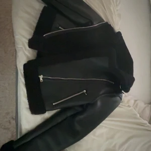 Svart teddyjacka från Zara med dragkedjor - Säljer en svart teddyjacka från Zara i storlek S. Jackan har bred krage, synliga silvriga dragkedjor och mjuka teddy-detaljer vid krage, ärmslut och nederkant. Perfekt för kalla dagar och ger en cool vibe till din outfit.