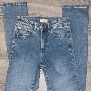 Blå jeansbyxor, strl 34 - Snygga blå jeansbyxor från Lindex i modellen Alba. Klassisk femficksdesign, normal passform och raka ben. Jeansen har bälteshällor, knapp och dragkedja framtill. Perfekta till en avslappnad stil och funkar året runt.