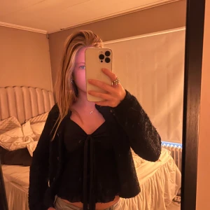 Svart linnetopp med knyt fram - Säljer en svart linnetopp med smala axelband och snygg knytning framtill. Toppen har en lätt volangkant nedtill och v-ringad urringning. Perfekt att styla med jeans eller kjol för en trendig look.