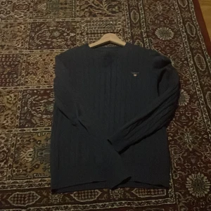 Mörkblå kabelstickad tröja från Gant - Säljer en mörkblå kabelstickad tröja från Gant i premium bomull. Tröjan har rund halsringning, diskret Gant-logo på bröstet och långa ärmar. Perfekt för dig som gillar klassisk och stilren look.