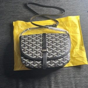 Svart axelväska  - Snygg svart axelväska från  med ikoniskt grafiskt mönster i vitt och beige. Väskan har justerbar axelrem, lock med spänne och detaljer i skinn. Perfekt storlek för det viktigaste och en riktigt stilren accessoar.