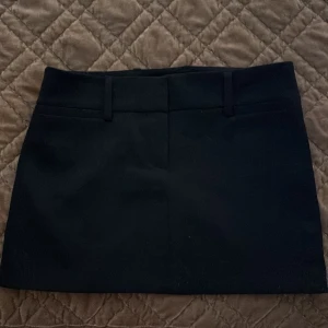 Svart kortkjol från Zara - Svart kortkjol från Zara med stilren design och bälteshällor i midjan. Kjolen har en rak passform och är tillverkad i ett slätt material som ger en snygg och enkel look. Perfekt för dig som gillar minimalistisk stil och vill ha en klassisk kjol i garderoben.