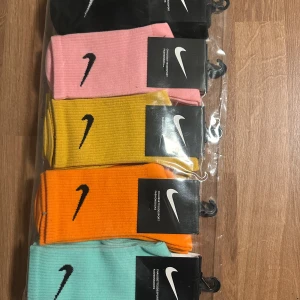  Nike strumpor i 10-pack. 5 färger! - Säljer ett 10-pack Nike strumpor i olika färger: svart, rosa, gul, orange och ljusblå. Strumporna är ribbade och har den klassiska Nike-loggan broderad på sidan. Perfekta för att addera lite färg till din outfit.