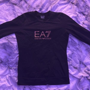 Svart långärmad tröja EA7 Armani - Svart långärmad tröja från EA7 Emporio Armani med tryckt logga i metallic på bröstet och ryggen. Slimmad passform och rund halsringning. Storlek S, men liten i storleken.