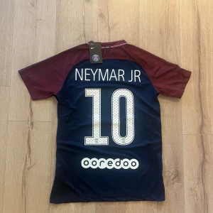 PSG Neymar Jr matchtröja Nike S - Paris Saint-Germain fotbollströja med Neymar Jr och nummer 10 på ryggen. Tröjan är marinblå med vinröda korta ärmar, PSG-emblem på bröstet och Fly Emirates-tryck. Tillverkad i lätt Dri-Fit material som andas, perfekt för träning eller match.