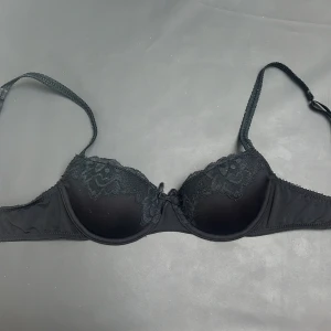 Svart spets-bh från Hunkemöller  - Snygg svart bh från Hunkemöller i storlek 70A . Kuporna har dekorativ spets med blommönster och en liten rosett framtill. Axelbanden är justerbara och den är från hunkemöller och har inga hål eller defekter.🫶