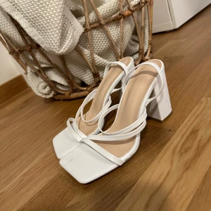 Vita klackar - Snygga vita sandaler. Skorna har tunna remmar som korsar foten och ger en modern look. Perfekta för dig som gillar stilrena och trendiga skor med en twist.