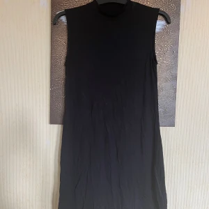 Svart ärmlös klänning Even&Odd - En svart, ärmlös klänning från Even&Odd med hög hals och rak passform. Klänningen är enkel och stilren, perfekt för dig som gillar minimalistisk stil. Tillverkad i mjuk bomull som känns skön mot huden.