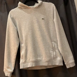 Grå hoodie från Lacoste - Snygg ljusgrå hoodie från Lacoste Sport med klassisk krokodillogga på bröstet. Mjuk och skön bomullsblandning. Nästan aldrig använd. Passar storlek 158 också.