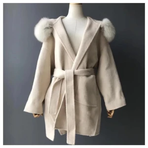 Beige kappa med huva och pälskant - Snygg beige kappa med huva och fluffiga pälskanter på axlarna. Jackan har bälte i midjan och stora fickor framtill. Perfekt till utekvällar eller fina midaggar. Tyvärr har den inte kommit till användning ens en ända gång så det blir sälj för mig. Köpt för 3899kr..