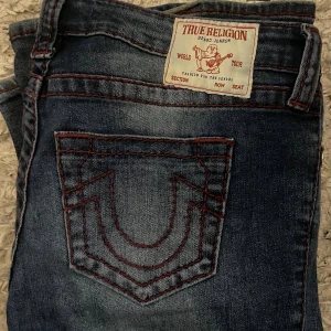 True religion jeans - Säljer dessa low waist bootcut True religion jeans med röda detaljer, köpta för 1399! De är slitna längst ner där bak, annars bra skick! Storlek 29 och de är väldigt stretchiga. Pris kan diskuteras🥰 Skriv för fler frågor osv!