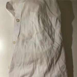 Vit skjorta och svarta kostymbyxor - Säljer en klassisk vit skjorta med bröstficka och knappar framtill, samt ett par svarta kostymbyxor med knapp och dragkedja i midjan. Perfekt för dig som gillar stilrena och enkla plagg. Skjortan är i bomull och byxorna har en rak passform.