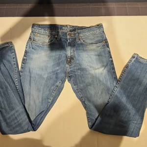 Blå jeans Grant W32 L34 - Säljer ett par klassiska blå jeans från Grant, modell 405. Jeansen har fem fickor, snygga kontrastsömmar och en läderpatch bak i midjan. Passformen är rak och materialet är slitstark denim. Perfekt för dig som gillar tidlös stil och vill ha jeans med lite längre ben.