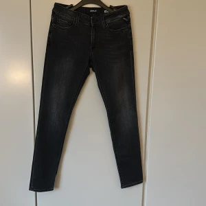 Svarta Replay jeans - Snygga svarta jeans från Replay med smal passform och klassisk femficksdesign. Jeansen har en mörk tvätt med subtila slitningar och raka ben. Perfekt för dig som gillar stilrena och moderna jeans med en cool vibe.
