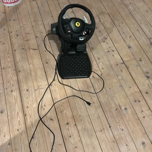 Thrustmaster Ferrari Racing Wheel - Thrustmaster Ferrari Racing Wheel med pedaler, USB-anslutning. Realistisk ratt med Ferrari-logo, flera knappar och paddlar. Passar till PC och spelkonsoler. Bra skick, inga synliga defekter eller slitage. Perfekt för racingentusiaster som vill ha en autentisk körupplevelse. Köpte varan föra året men inte användits mycket är fortfarande i bra skick