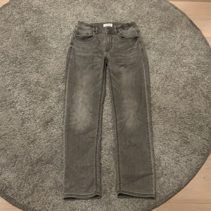 Grå jeans Staffan från Lindex - Snygga grå jeans från Lindex, modell Staffan, med klassisk femficksdesign och raka ben. Jeansen har normal passform och är tillverkade i mjukt denim-material. Perfekta för dig som gillar enkel och stilren look.