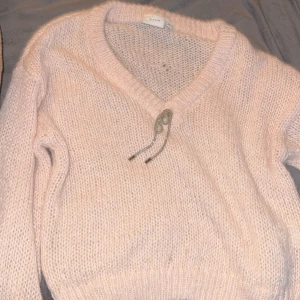 Ljusrosa stickad tröja från VILA - Mysig ljusrosa stickad tröja från VILA med v-ringad hals och långa ärmar. Tröjan har en mjuk och fluffig känsla, perfekt för kyliga dagar. Snygg detalj med snörning vid halsen som ger en extra touch. Har aldrig använts 💕