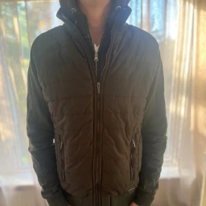 Cardigan  - Säljer en grön quiltad bomberjacka med hög krage och dubbla dragkedjor framtill. Jackan har ribbade muddar vid ärmslut och nederkant samt två fickor med dragkedja. Perfekt för dig som gillar en stilren och sportig look. Skriv för mer info🌟