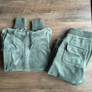 Grönt velour set från Juicy Couture - Grönt set från Juicy Couture i velour med huva, snörning och dragkedja med J-logga. Metallen har trillat av snöret på tröjan och byxan. Se bild ovan