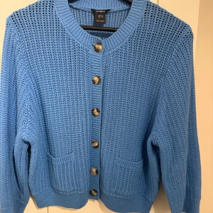 Blå stickad kofta - Lindex - Säljer en blå stickad kofta från Lindex med snyggt hålmönster, ribbade muddar och två fickor framtill. Koftan har stora knappar och är långärmad.Den är använd några gånger men har inga defekter och är i mycket bra skick. Den har en superfin blå färg och passar perfekt till både hösten och vintern🩵