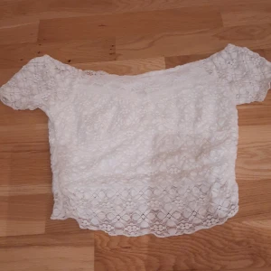 Vit spetsblus från Romwe XS - Supersöt vit blus från Romwe i storlek XS. Blusen har korta ärmar och är täckt av blommig spets med fodrad insida. Offshoulder-modell som ger en romantisk vibe och passar perfekt till ljusa dagar. Spetsen har fina detaljer och blusen är croppad i modellen.