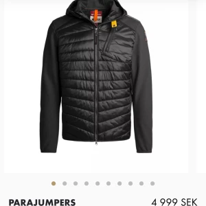 Svart pufferjacka från Parajumpers - Svart pufferjacka från Parajumpers med quiltad front, huva och dragkedja. Jackan har en gul detalj vid halsen och en bröstficka med dragkedja. Ärmarna är släta och materialet är en mix av polyester och syntet. Perfekt för kyliga dagar.