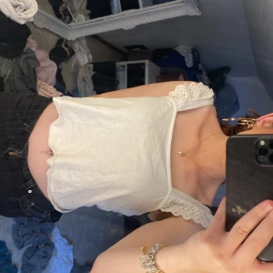 Vit linnetopp med spets från H&M - Säljer en söt vit topp från H&M i storlek M. Toppen har breda axelband med broderad spets och en rak, croppad passform. Perfekt för varma dagar och enkel att matcha med jeans eller kjol. Materialet är mjukt och bekvämt. Passar även folk med storlek s