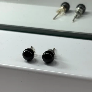 Svarta runda örhängen i silverfärg - Snygga örhängen med rund svart pärla och silverfärgad stift. Två olika pluppar för ena borttappad.