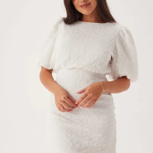 Vit kort klänning med puffärm och rosett - Superfin vit studentklänning med puffärmar och snygg rosettdetalj i ryggen. Klänningen har en strukturerad yta och markerad midja. Använd en gång 😀Skulle säga att det är en stor M