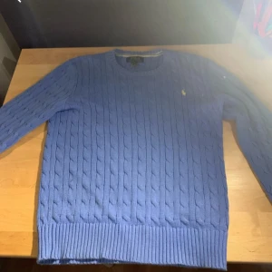 Blå kabelstickad tröja Polo Ralph Lauren - Bara använd runt 2-3 gånger jätte fint skick. Snygg blå kabelstickad tröja från Polo Ralph Lauren. Med en QR cod som man kan scanna som bevisar att det är äkta vara. storlek 14-16 åringar. Köpte för 2200 säljer nu för endast 1399