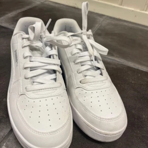 Vita sneakers från Puma - Fräscha vita sneakers från Puma med klassisk låg siluett och rund tå. Skorna har snygga detaljer som perforering på tån, tydlig Puma-logga på sidan och bak, samt vit snörning. Tillverkade i syntetmaterial med skinnlook och platt sula för skön komfort. Använda 1 gång och nypris är 599. Pris kan diskuteras 