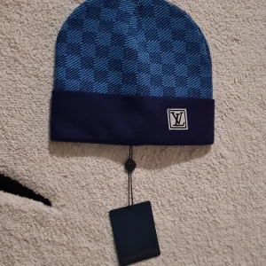 Blå rutig mössa från L&V - Snygg blå mössa från L&V med klassiskt rutigt mönster i två nyanser av blått. Mössan har en bred, mörkblå uppvikt kant med L&V-logga framtill. Tillverkad i mjukt material som passar perfekt för kyliga dagar. En stilren accessoar för dig som gillar exklusiva märken.