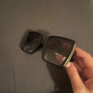 Svarta och guldiga solglasögon - Två par solglasögon köpta i Italen! Ena paret har stora, fyrkantiga svarta bågar med gulddetalj på sidan – riktigt statement. Andra paret har tunna, ovala guldiga metallbågar med mörka glas och bruna skalmar. 