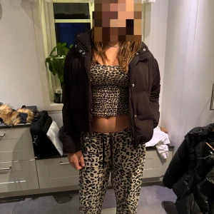 Svart croppad pufferjacka - Säljer en svart, croppad pufferjacka med hög krage och breda kanaler. Jackan har en enkel design utan synliga loggor och stängs med dragkedja framtill. Perfekt för dig som gillar en stilren och trendig look under kyliga dagar.